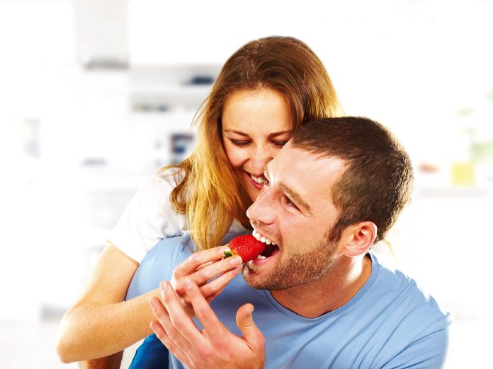 Happy young couple eating strawberries together.