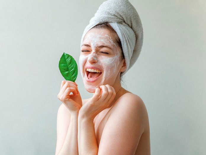 Woman face with green leaf and cream or nourishing mask