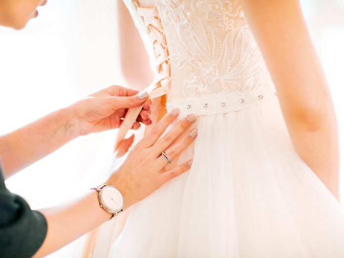 Bridesmaid helping the bride to put her wedding dress on