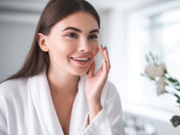 Satisfied girl doing face treatment in morning