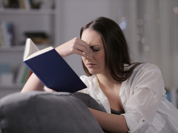 Lady suffering eyestrain reading book in the night