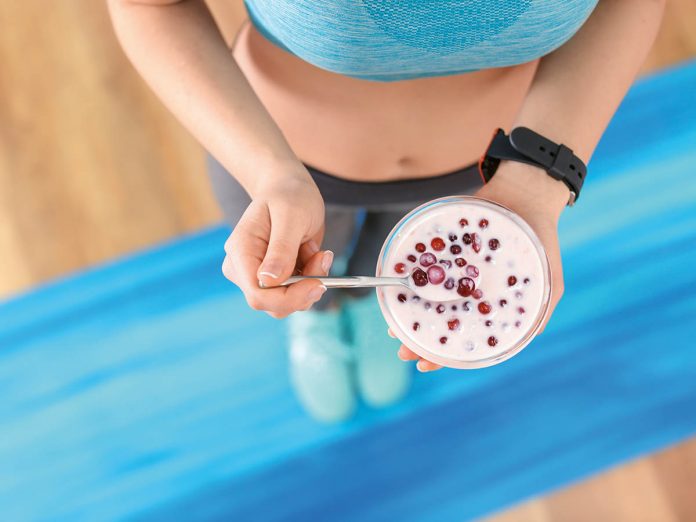 Sporty young woman eating yogurt with berries after fitness trai