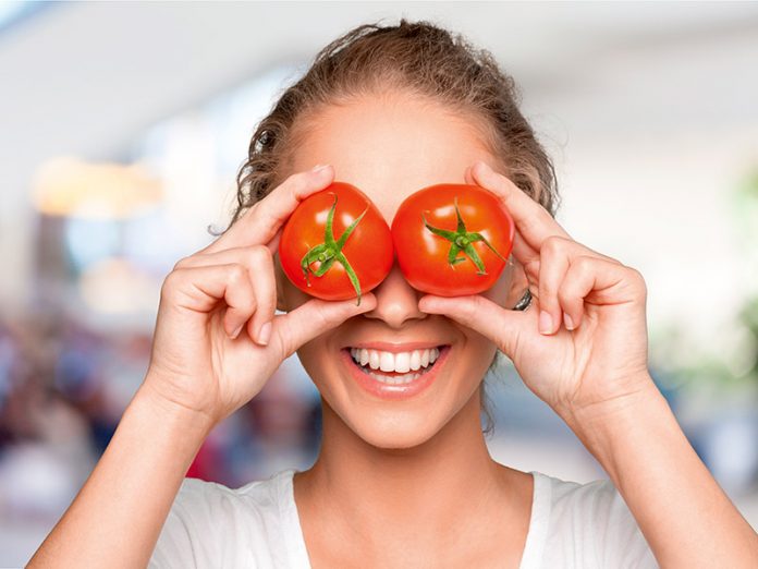 Beautiful laughing woman holding two ripe tomatoes before her ey
