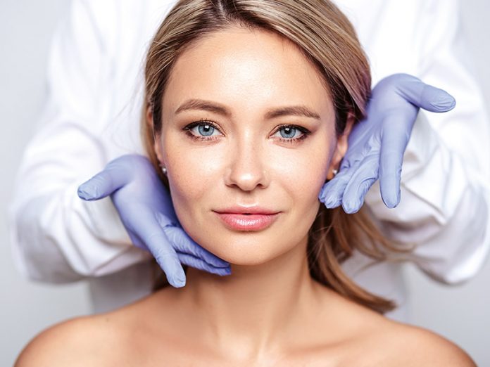 Close up portrait of young blonde woman with cosmetologyst hands
