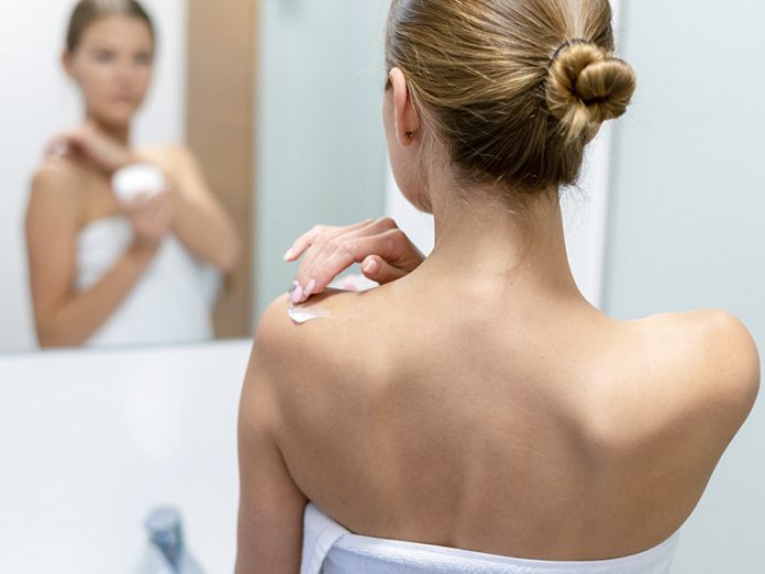 Woman applying body cream on shoulder in bathroom