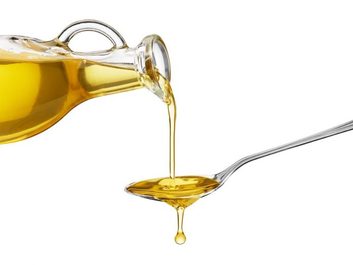 Oil being poured from a large bottle onto a spoon