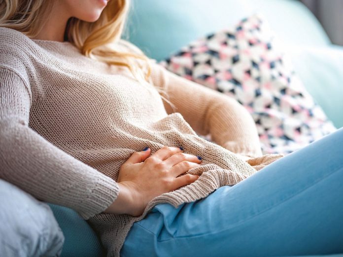 Young woman suffering from abdominal pain while sitting on sofa