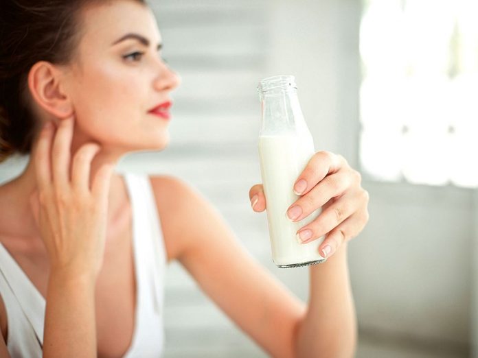 Young woman holding a bottle of milk in her hand. Set of brunette girl wearing white singlet in white room with window on background